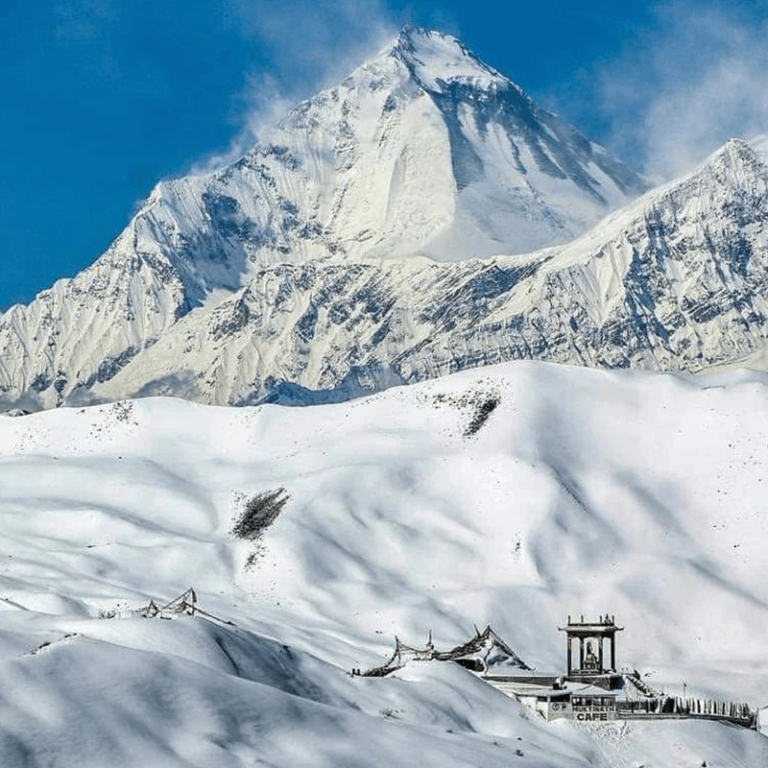 A snowy mountain with a small building in the middle, surrounded by a serene winter landscape.